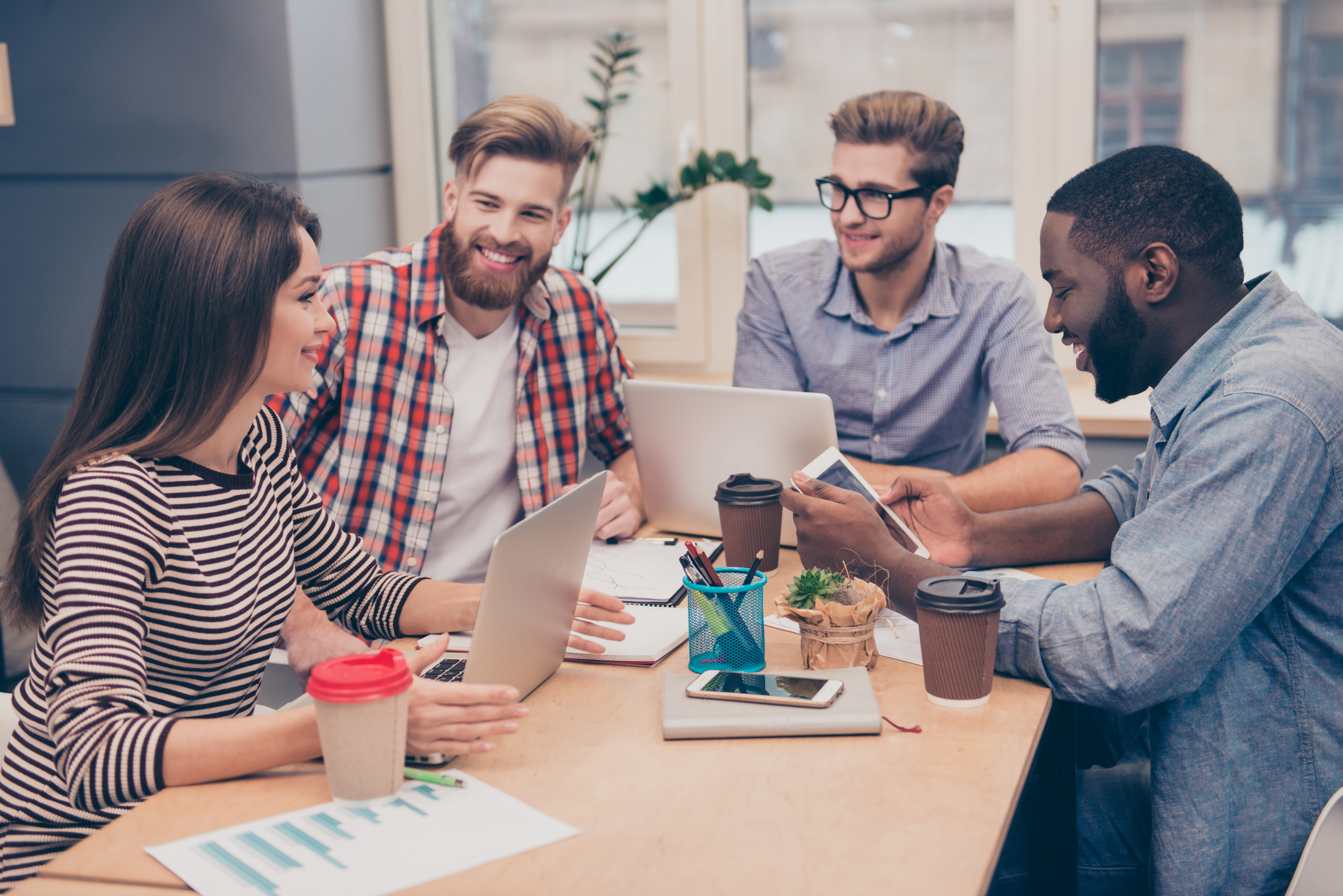 Vier Menschen in einem modernen Büro im inspirierenden Austausch – eine Führungskraft und Mitarbeitende gestalten gemeinsam sinnvolle Arbeit auf Basis eines klaren Leitbilds